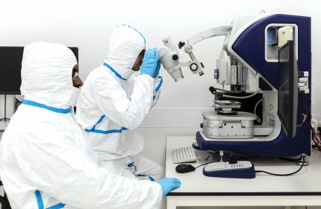 Scientists in protective suits looking into a microscope