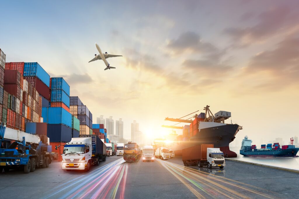 A port scene shows cargo ships, trucks, and stacked containers. An airplane is flying overhead against a sunset sky, with city skyscrapers visible in the background.